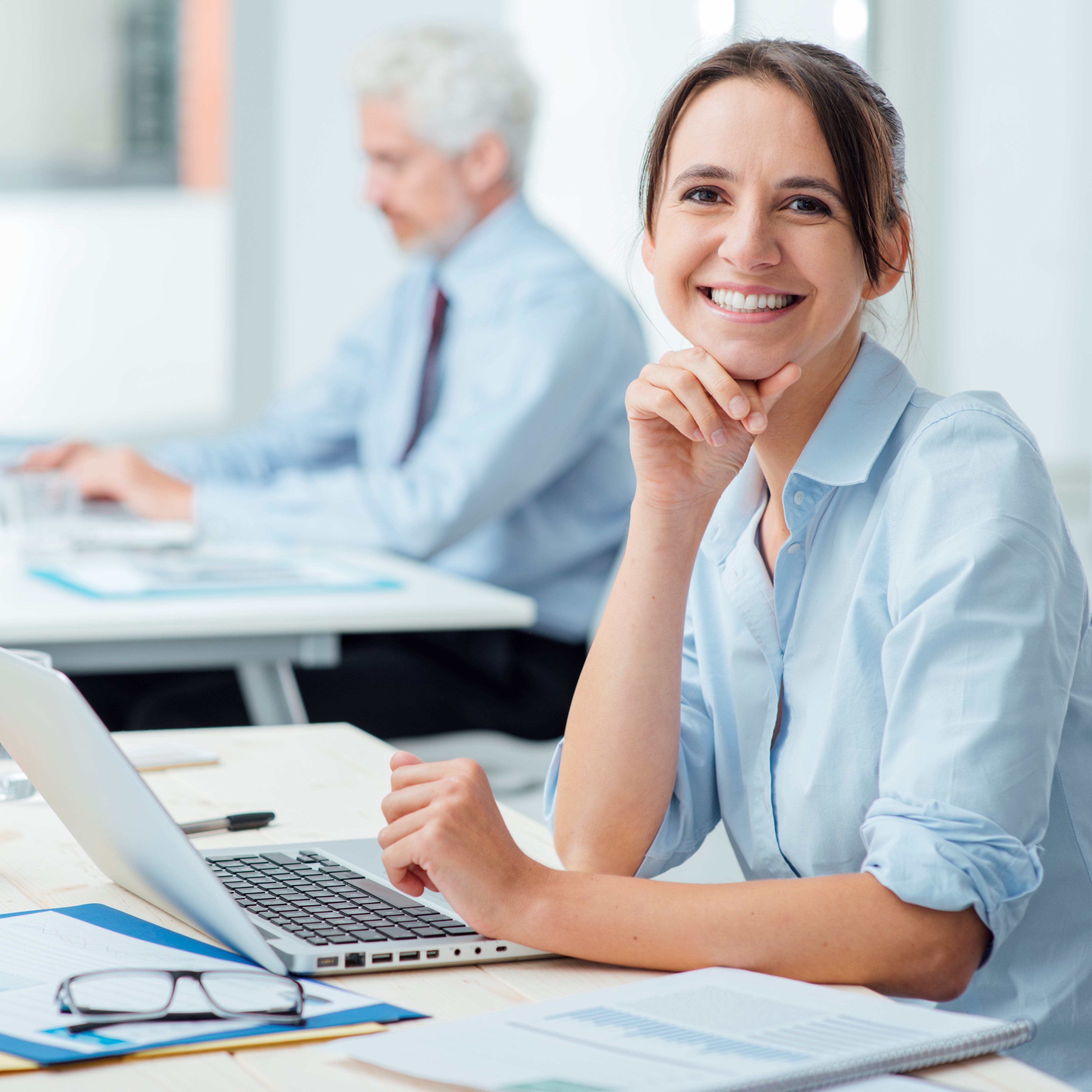 Smiling business woman at work Smiling young business woman sitting at office desk and working with a laptop, she is looking at camera